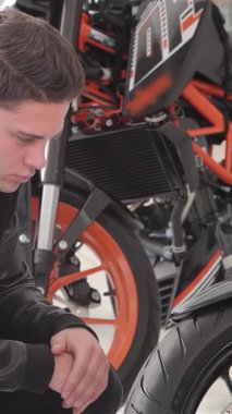 Neşeli beyaz bir adam çarpan siyah bir motosikletin yanında diz çöker ve gülümseyen bir gülümsemeyle baş parmağını kaldırır. Heyecanı, motosikletlerin gösterişli tasarımlarına ve güçlü özelliklerine hayran kalarak, macera ve motosiklet heyecanının somutlaştırılmasıyla bariz bir şekilde hissediliyor.