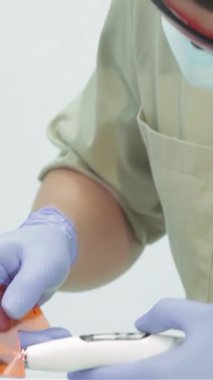 Parlak ve modern bir diş kliniğinde, kendini adamış bir diş hekimi genç bir kadının dişlerine titizlikle fotopolimer foku uygular ve ultraviyole lambayı kesin tedavi için kullanır. Bu yakın çekim profesyonelliği ve özeni vurguluyor.