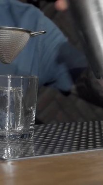 Yetenekli bir erkek barmen, fevkalade bir miksoloji yeteneğini sergilemek için süzgeçten geçip şık bir bardağa kremalı kokteyl döker. Sıcak, davetkar bar atmosferi, retro dekoru ve yumuşak ışıklandırmasıyla, canlı bir ışık yaratıyor.