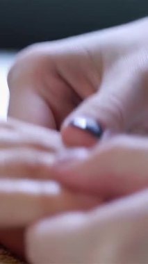 Yakın çekim bir güzellik uzmanının ellerini rahatlatıcı bir hareketle müşterinin parmaklarına nazikçe masaj yaparken, sakin bir manikür salonu atmosferiyle sarmaladığını gösterir. Manikürlü tırnakların ve yumuşak teninin altını çizerek lüks ve rahatlatıcı bir sahne yayıyor.