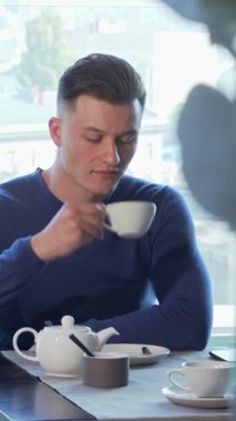Hoş mavi kazaklı yakışıklı genç bir adam sıcak bir fincan çayın tadını çıkarıyor, canlı bir şehir manzarasına dalgın dalgın dışarı bakıyor. Bu huzurlu an, sofistike ve rahatlamayı simgeler. Kahvaltı toplantısı ya da sessiz tefekkür için idealdir.