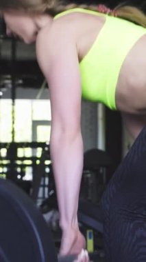 Bu büyüleyici arka planda, çarpıcı neon bir üst ve parlak siyah tozluklu kararlı bir sporcu modern bir spor salonunda ağır bir halteri kaldırırken heykel şeklindeki vücudunu sergiliyor. Enerjik atmosfer enerjiyle doludur.