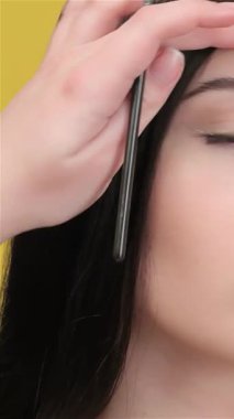 Yetenekli bir vizör, göz makyajına hazırlanırken, muhteşem bir Asyalı kadının saçını titizlikle şekillendirir. Canlı sarı arkaplan enerji yayıyor, modelleri vurguluyor dengeli ifade ve sanatsal