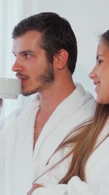 Pofuduk beyaz bornozlara sarılı neşeli bir çift, pencereden dışarı sevgiyle bakıyor, kahkahaları lüks otel odasında yankılanıyor. Güneş ışığı perdelerin arasında dans eder, şefkatli gülümsemelerine sıcak bir parıltı saçar, rüya gibi bir gülümseme yaratır.