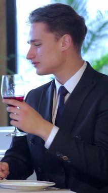 Şık genç bir çift zarif bir restoranda yıldönümlerini kutluyor. İçtenlikle kadeh kaldırarak zengin kırmızı şarap kadehlerini kaldırıyorlar. Samimi ortam, yumuşak ışıklandırma ve çarpıcı bir çiçek süsü ile güzelce tamamlanmış.