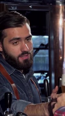 Yakışıklı, sakallı bir barmen, kremalı koyu bir biradan zevk alır. Kutlama kadehinde köpüklü bardağı kaldıran bir müşteriyle nişanlanırken gözleri neşeyle parlar. Bu canlı bar sahnesi sıcaklığı ve dostluğu yansıtıyor, şenlik ruhunu somutlaştırıyor.