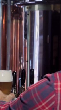 Karizmatik sakallı bir barmen, kutlama için kadehini kaldıran müşterisiyle neşeli bir kadeh tokuştururken altın köpüklü biranın tadını çıkarır. Bu canlı bar sahnesi sıcaklığı ve dostluğu yansıtıyor, gece hayatının şenlikli ruhunu ve