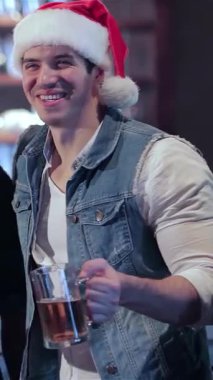 Neşeli bir barda, Noel Baba şapkası takan iki arkadaş bayram ruhunu somutlaştırmak için buzlu bira bardaklarını kaldırır. Arka planda neşeli barmen ışıkları, kahkahalarla, arkadaşlıkla dolu neşeli atmosferi güçlendiriyor.