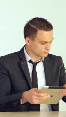 Keskin, özel dikim takım elbiseli kararlı genç bir işadamı bir elinde zarif bir tablet tutarken, dikkatle telefona cevap veriyor, profesyonellik ve hırsı somutlaştırıyor. Parlak, modern ofis arkaplanı üretkenlik ve odaklanma atmosferi yayıyor.