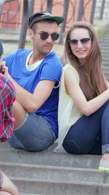 İki şık genç arkadaş, bir erkek ve bir kadın, güneşli basamaklarda neşeli bir fotoğraf için poz verirken kahkahalarını paylaşıyorlar. Bu canlı sahne mutluluk ve bağlantı yayar, kaygısız ruhlarını güzel bir yaz gününde vurgular.