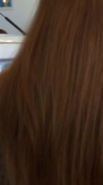 Dalgalı kahverengi saçlı zarif bir genç kadın, galerideki modern bir arabanın içinde elleri direksiyonda yavaşça dinleniyor. Üst düzey araçlarla süslenmiş parlak, lüks sergi salonu davetkar bir atmosfer yayıyor.