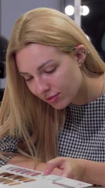 Şık bir kuaför salonundaki canlı bir saç stili kataloğuna hevesle göz atan zarif, genç bir kadın. Parlak, modern ortam heyecan ve kendine dikkat duygusu yayıyor. Çarpıcı bir arzuyu mükemmel bir şekilde yakalıyor.