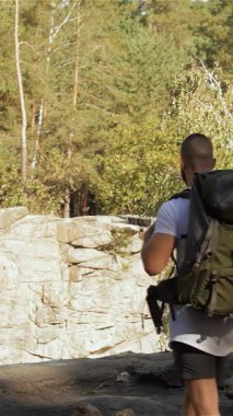 Uçurumun kenarında el ele duran genç bir çift, göz kamaştırıcı dağ manzaraları ve yemyeşil manzaralarla çevrili. Esmer adam ve kadın, her ikisi de canlı yürüyüş kıyafetleri içinde, sıska kız parmaklarının ucunda dururken yürekten kucaklaşırlar.