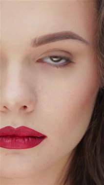 Bu büyüleyici yakın plan gösterileri, parlak esmer saçlı ve koyu kırmızı dudaklı beyaz bir kadın, parlak siyah bir fonda sergileniyor. Kusursuz cildi saflıkla parlarken yoğun bakışları ve yumuşak gülüşü özgüven ve cazibe yayıyor.