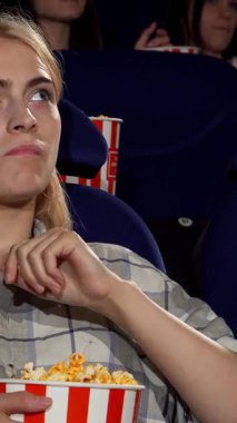 Çekici bir genç kadın, düşünceli bir ifadeyle, sinemada sürükleyici bir filme dalmışken tereyağlı patlamış mısıra daldı. Canlı, loş ışıklı tiyatro heyecanla uğulduyor, mükemmel bir hafta sonu kaçışı için davetkar bir atmosfer yaratıyor.