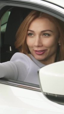 Uzun, dalgalı saçları olan ışıldayan genç bir kadın yeni şık arabasından selfie çekerken mutluluk saçıyor. Canlı sahne, onun heyecanını ve yeni mülkiyetinin heyecanını yakalıyor, modern teknolojiyi zevkle harmanlıyor.