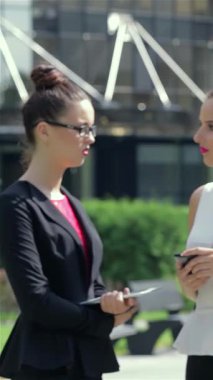 Gösterişli, siyah bir ceket giymiş dengeli genç bir iş kadını tabletiyle açık havada derinden ilgilenirken, meslektaşları arka planda canlı canlı sohbet ediyorlar. Bu canlı sahne modern iş işbirliğinin nabzını özetliyor.