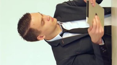 Keskin, özel dikim takım elbiseli kararlı genç bir işadamı bir elinde zarif bir tablet tutarken, dikkatle telefona cevap veriyor, profesyonellik ve hırsı somutlaştırıyor. Parlak, modern ofis arkaplanı üretkenlik ve odaklanma atmosferi yayıyor.