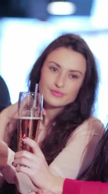 Canlı bir üçlü genç arkadaş, iki kadın ve bir erkek, coşkulu bir barda bardaklarını kaldırarak en sevdikleri futbol takımının zaferini kutluyorlar. Elektrik atmosferi kahkahalarla ve bar ışıklarıyla dolu.