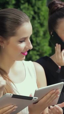 Üç dinamik iş kadını şık bir ofisin önünde durup tableti incelerken etkileyici başarılarını tartışırlar. Işıl ışıl gülümsemeleri ve şık kıyafetleri, canlı bir işbirliği ve başarı atmosferi yaratıyor.