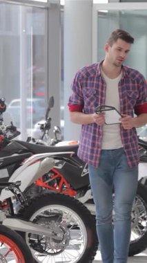 Hayat dolu bir motosiklet salonunda, kendine güvenen bir satıcı ve hevesli bir müşteri sıkı bir tokalaşmayla heyecan verici bir anlaşma yapar. Göz kamaştırıcı gösterişli çapraz motosikletlerle çevrili, parlak gösteri salonu enerjiyle uğulduyor, heyecanı yansıtıyor.