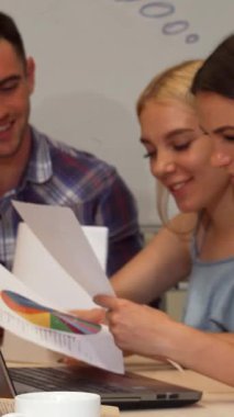 Şık, sarı saçlı, hayat dolu genç bir iş kadını şık, modern bir ofisteki iş arkadaşları tarafından çevrelenmiş akıllı telefonuyla mesajlaşıyor. Canlı atmosfer yaratıcılık ve takım çalışması ile yüklü. Fikir alışverişinde bulunuyorlar.