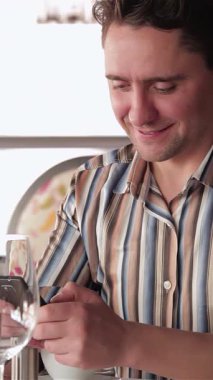 Sıcak ışıklandırılmış bir kafede, rahat giyimli genç bir işadamı dizüstü bilgisayarı üzerinde çalışırken sevinçle ışıldıyor, duygusal bir bağ ve üretkenlik anını somutlaştırıyor. Yakınlarda, akıllı telefonuna kendini kaptırmış başka bir adam daha canlı bir atmosfere...