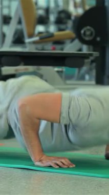 Orta Doğu kökenli odaklanmış genç bir adam şık, modern bir spor salonundaki canlı yeşil bir spor minderinin üzerinde enerjik bir şekilde şınav çekiyor. Yoğun ifadesi ve iyi tanımlanmış kasları spor yapmaya olan bağlılığını yansıtıyor.