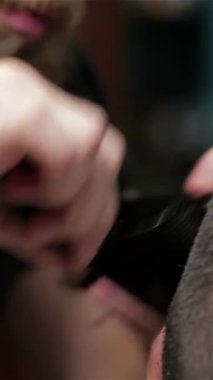 Bir berber dükkanında, titiz bir berber, sakallı bir adamın saçını ustalıkla şekillendirir, hassasiyetini ve sanatını ön plana çıkarır. Parlak atmosfer makas kesme sesleri ve zengin tımar ürünleri aromasıyla uğulduyor.