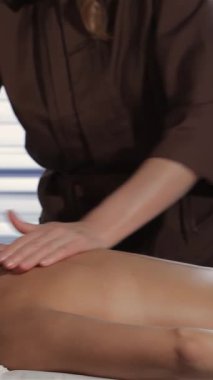 Barışçıl bir güzellik salonunda, profesyonel bir masör, yumuşak bir masaj masasına sarılı, rahat bir beyaz kadının sırtına ustalıkla masaj yapar. Yumuşak ışık ve zarif dekorun hafif parıltısı rahatlatıcı atmosferi güçlendirir.