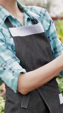 Şık kot önlüklü neşeli sarışın bir çiçekçi uzun, zarif saplı ve canlı bir bahçe merkezinde çarpıcı kırmızı çiçekleri olan nefes kesici bir orkideyi sevgiyle inceliyor. Rengarenk çiçeklerden oluşan canlı bir duvar halısıyla çevrelenmiş, sarhoş edici bir şekilde eğleniyor.