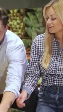 Şık sakallı, genç, beyaz bir adam canlı bir süpermarkette ışıldayan sarışın kız arkadaşına üç tane kırmızı domates veriyor. Lezzetli etkileşimleri, canlı üretim koridorlarında gezinirken sıcaklık ve bağlantı yayar.