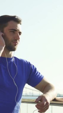 Düşük açılı bir bakış açısı, canlı mavi gömlekli, yakışıklı, sakallı bir adamı enerji veren bir egzersizden sonra kendini müziğe daldırırken mutlulukla gülümserken yakalar. Bu canlandırıcı sahne pozitifliği ve sükuneti yansıtıyor.