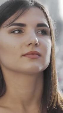 Güzel genç bir kadın, hareketli bir şehrin enerjik enerjisinin ortasında birini beklerken düşünceli bir şekilde uzaklara bakar. Yumuşak güneş ışığı çarpıcı özelliklerini ön plana çıkarıyor. Doğal güzelliğini gösteren büyüleyici bir atmosfer yaratıyor.