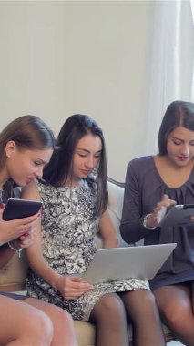 Üç zarif genç kadın şık bir kanepeye rahatça oturmuş sürpriz indirimler için aletlerini hevesle karıştırıyorlar. Işıl ışıl gülümsemeleri ve şık kıyafetleri heyecan verici bir neşe ve dostluk atmosferi yaratarak online alışverişi...