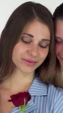 Büyüleyici gözleri olan güzel bir kadın tatlı kırmızı bir gülün tatlı kokusunu soluyor, sıcak bir gülümsemeyle yanında duran büyüleyici erkek arkadaşı tarafından sevgiyle sunuluyor. Bu samimi an sevgi ve neşe saçıyor, onu ideal kılıyor.