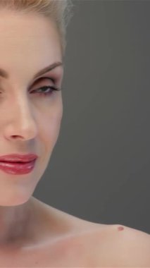 Nefes kesici sarışın bir kadın büyüleyici bakışlarıyla hayranlık saçıyor. Kusursuz cildi, soluk gri bir zemine hafifçe parlıyor. Bu portre güzelliğin ve zarafetin özünü yakalıyor, narin gülümsemesini ve narin özelliklerini vurguluyor.