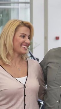 Neşeli, olgun bir çift, yeni arabalarını lüks bir galeride satın aldıktan sonra sevinçten havalara uçarak içten bir kucaklaşmayı ve coşkulu bir beşlik çakmayı paylaşıyor. Parlak araçlar ve modern bir sergi salonu ile çevrelenmiş, heyecanları heyecan verici.