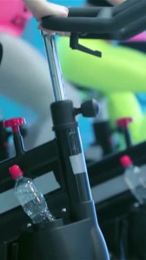 Hareketli bir spor salonu ortamında hareketsiz bisikletler, enerji ve coşku saçan hareketsiz bisiklet pedallarının dinamik dörtlüsü. Hareketli spor kıyafetleri ve azimli ifadeleri güçlü bir dostluk bağını ve paylaşımı yansıtıyor.