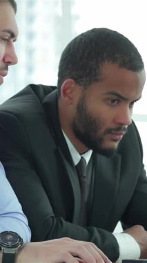 Biri şık takım elbiseli, diğeri de şık gömlekli iki kararlı iş adamı, şık ve çağdaş bir ofis masasında dizüstü bilgisayarın üzerinde derin bir işbirliği içindeler. Yoğun ifadeleri ve odaklanmış tavırları takım çalışmasının özünü vurguluyor.