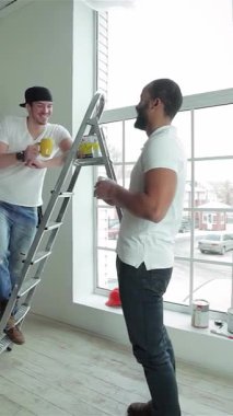 İki neşeli işçi aynı neşeli anı paylaşıyor. Güneşli, yenilenmiş bir dairede aperatiflerin ve kahkahaların tadını çıkarıyorlar. Bir adam, neşeyle bir merdivene tünemiş, ellerini meslektaşına boyuyor, takım çalışmasını ve arkadaşlığını canlı, havadar bir mekanda somutlaştırıyor.