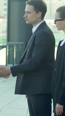 Parlak siyah takım elbiseli güler yüzlü iş adamlarından oluşan canlı bir üçlü, canlı bir şehir manzarasının arka planına karşı sıkı bir tokalaşmaya giriyorlar. Bu enerjik sahne, işbirliği ve başarı ruhunu somutlaştırıyor. Oluşturdukları zaman heyecan yayıyor.