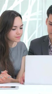 Genç, çekici bir iş adamı ve kadın yoğun bir şekilde parlak ve modern bir ofiste fikir ve strateji alışverişinde bulunan parlak bir dizüstü bilgisayara odaklanmış durumdalar. Kadınlar düşünceli bir şekilde başlarını sallıyor ve erkekler de işbirlikçi ruhlarını vurguluyor.