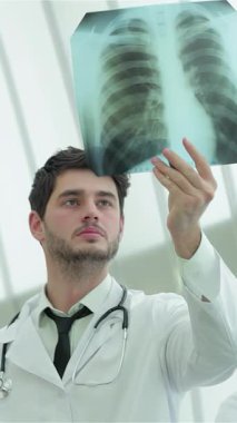 Crisp beyaz önlük ve steteskop giymiş odaklanmış bir erkek doktor, sigara içmenin tehlikelerini gösteren bir akciğer röntgeni çekiyor. Yoğun bakışları ve modern klinik arka planı sağlık farkındalığının önemini vurguluyor.