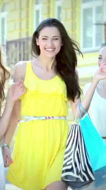 Işıl ışıl yaz kıyafetleri giymiş üç ışıl ışıl kız, güneşli bir sokakta gururla geziyorlar şık alışveriş çantalarını sergiliyorlar. Bulaşıcı kahkahaları ve parlak gülümsemeleri, dostluk ruhunu ve alışverişin heyecanını temsil eder.