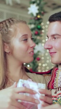 Yürek ısıtan bir sahnede, genç bir çift yumuşak bir battaniyenin altına kıvrılır, birbirlerine güzel hediyeler verirler, neşe dolu bir bekleyişle. Şık süveterleri ve eşarpları parıldayan ışıkları ve şenlikli süslemeleri tamamlayarak büyüleyici bir şey yaratıyor.