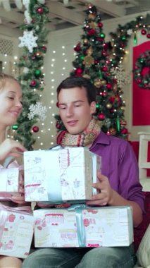 Sıcak süveter ve eşarplara sarılı neşeli bir çift, göz alıcı ışıklar ve canlı bir ağaçla süslenmiş büyüleyici bir Noel odasında birbirlerine güzel paketlenmiş hediyeler veriyorlar. Bu iç açıcı sahne aşk ve tatil ruhunu yansıtıyor.