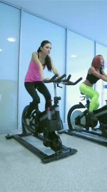 Enerjiyle dolu hareketli bir spor salonunda, dinamik bir arkadaş grubu durgun bisikletlerin üzerinde yoğun bir şekilde pedal çeviriyor, ifadeleri odak ve kararlılığı yansıtıyor. Renkli spor kıyafetleri giyip, yoldaşlık ve motivasyon yayıyorlar.