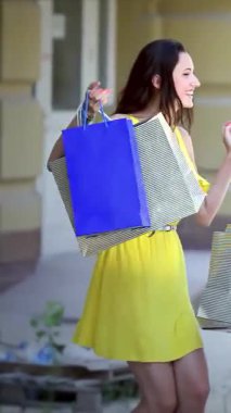 Parlak sarı elbiseli şık bir kız heyecanla atlıyor, renkli alışveriş çantalarını güneşli bir şehir zeminine yapıştırıyor. Onun ışıl ışıl gülüşü ve kaygısız ruhu arkadaşlığın ve sevincin özünü yakalıyor, perakendeciliğin heyecanını kutluyor.