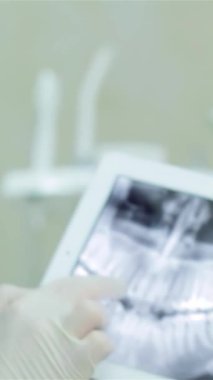 Zarif, modern bir diş kliniğinde, kendini işine adamış mavi önlüklü bir diş hekimi bir tablette hastanın dişlerinin detaylı röntgenine dikkatle işaret ediyor. Bu dönüm noktası ileri teknoloji ve uzman tedavisinin birleşiminin altını çiziyor.